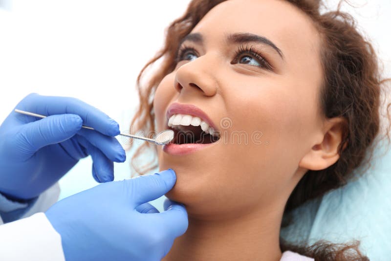 Dentist examining African-American woman`s teeth with mirror in hospital. Dentist examining African-American woman`s teeth with mirror in hospital